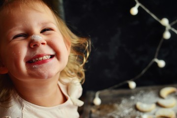 Portrait of a beautiful baby 2-3 years old. The girl has a nose in flour and icing sugar. A girl is preparing New Year and Christmas cookies. Food and baby in the frame. Beautiful girl smiles happily.