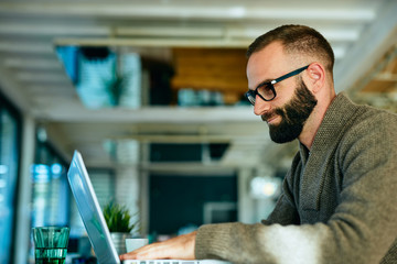 Attractive bearded man working on laptop in a cafe	