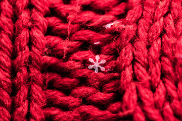 Macrophotography of snowflakes on a red knitted fabric with a large knit