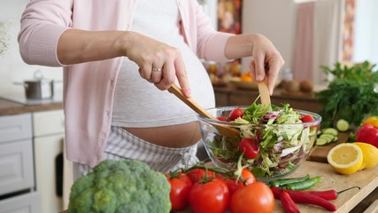 Pregnant Woman Mixing Fresh Green Salad On Kitchen. Closeup. - obrazy, fototapety, plakaty