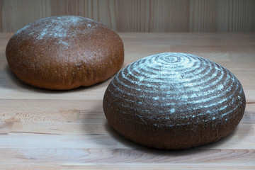 two round loaves of rye and wheat bread on a wooden background