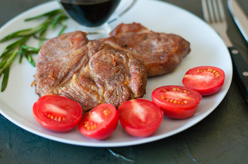 Fragrant pork meat steaks with spices, tomatoes and sauce, on a gray plate, on a dark concrete background, close-up