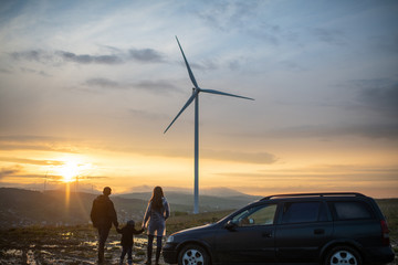 Happy family at sunset. father, mother and son looking at the wind turbine