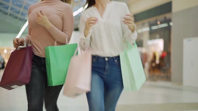 Medium shot of two unrecognizable faceless shopaholic women with shopping bags running along mall hurrying to make purchases on sale day