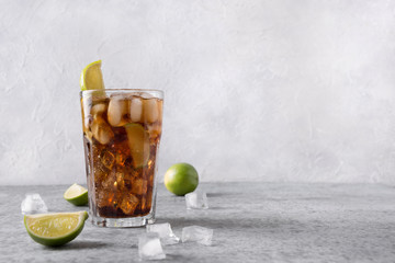 Cocktail Cuba Libre or long island iced tea with rom, cola, lime and ice in glass on grey stone...