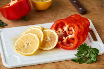 Slices of lemon and red bell pepper on a white cutting board