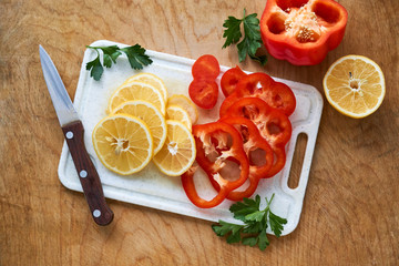 Slices of lemon and red bell pepper on a white cutting board