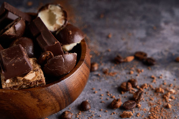 broken black and white chocolate in wooden bowl. Pieces of chocolates on a gray stone table