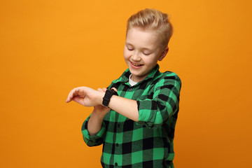 Happy little boy with a smartwatch. Beautiful smiling caucasian boy in a green shirt on a yellow background. Horizontal,  straight ahead.