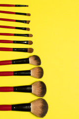 Set of red makeup brushes on yellow background 