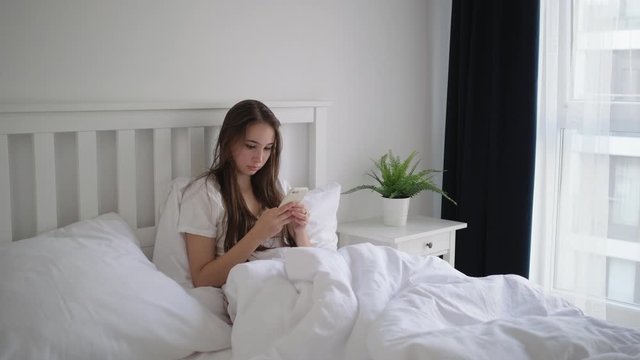 woman is using smartphone lying in bed in morning time