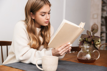 Image of nice caucasian woman reading book and drinking tea