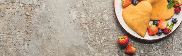 top view of heart shaped pancakes with berries on grey concrete surface, panoramic shot