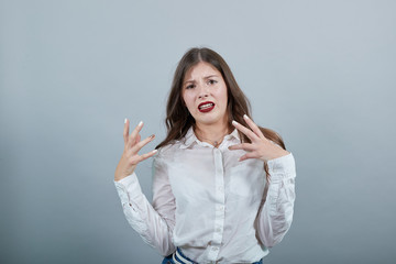 Charming young woman in fashion white shirt spreads hands, isolated on gray background in studio,...