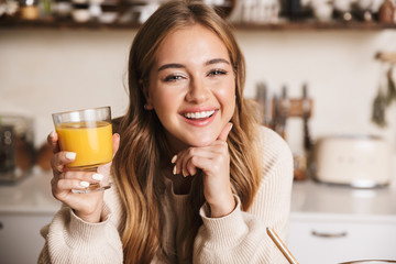 Image of smiling cute woman drinking juice while making lunch