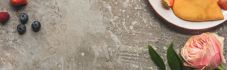 top view of heart shaped pancakes with berries on grey concrete surface near rose, panoramic shot