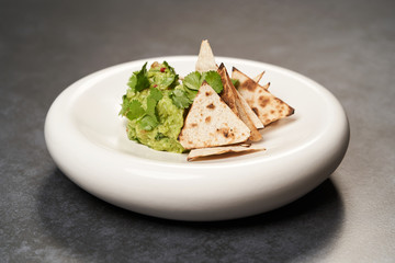 Guacamole with pita chips on white plate. Chef's signature dish