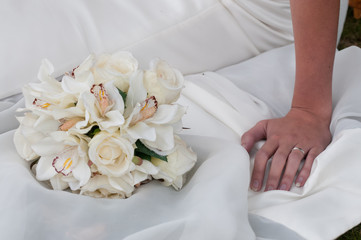 Close view of a wedding bouquet with bride's hand and ring against her wedding dress.Image