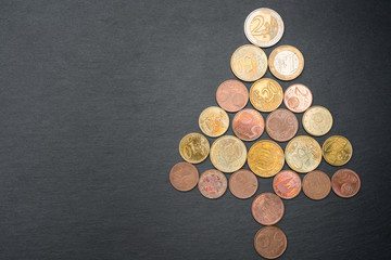 Christmas tree made out of Euro coins on dark black slate plate background. Copy space on the left. Flat lay top view.