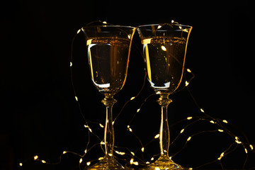 Two glasses with champagne sparkling wine on a dark background and sparkling bokeh. Atmosphere of celebration, magic and happiness.