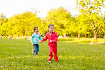 Fototapeta premium Children run on the green grass holding hands. Girls running around the lawn with grass playing with splashes of water to water plants.