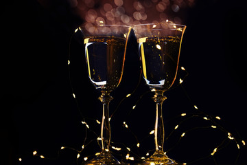 Two glasses with champagne sparkling wine on a dark background and sparkling bokeh. Atmosphere of celebration, magic and happiness.