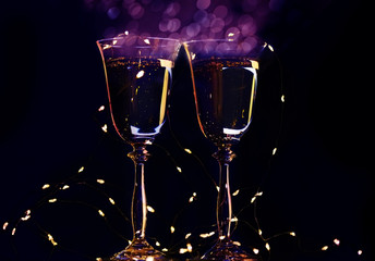 Two glasses with champagne sparkling wine on a dark background and sparkling bokeh. Atmosphere of celebration, magic and happiness.