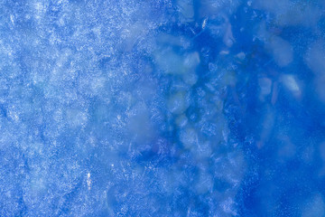 blue texture of an ice surface with pure azure water ,cold snow cryslallized wall background ,winter frozen lake side close up , abstract macro wallpaper
