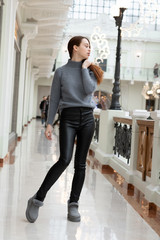 European tall girl with long red hair in black leather pants, gray uggs and a fluffy sweater posing in a shopping gallery near boutiques