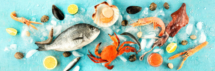 Fish and seafood panorama, a flatlay overhead shot on a blue background. Fresh fish, shrimps and...