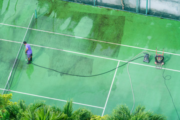 A man washes a tennis court from a hose.