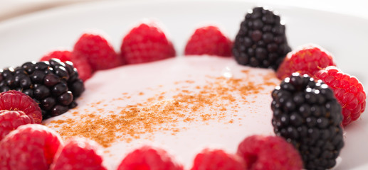 raspberries and blackberries laid out on a white plate in circle with yogurt and cinnamon
