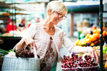 Picture of mature woman at marketplace buying vegetables