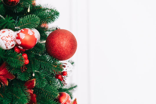 A fragment of a Christmas tree decorated with red balls on a white wall background