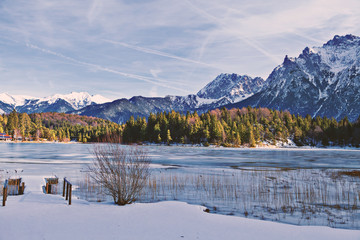 Zugefrorener Bergsee mit steilen Felswänden im Hintergrund und verschneiter Landschaft