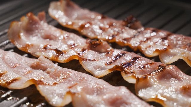 Pieces of bacon are fried in a pan. The concept of fatty and junk food, a source of trans fats and cholesterol. Close-up
