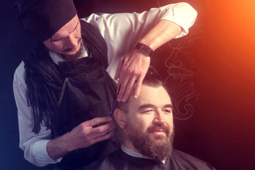 The barber cuts a man with a beard. Unique haircut.