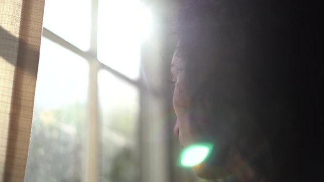 Young attractive woman looking out the window on a bright day with shunshine coming in the window - focus pull from woman to window - melancholy mood