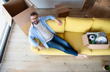 Top view of mature man with boxes moving in new house, relaxing on sofa.