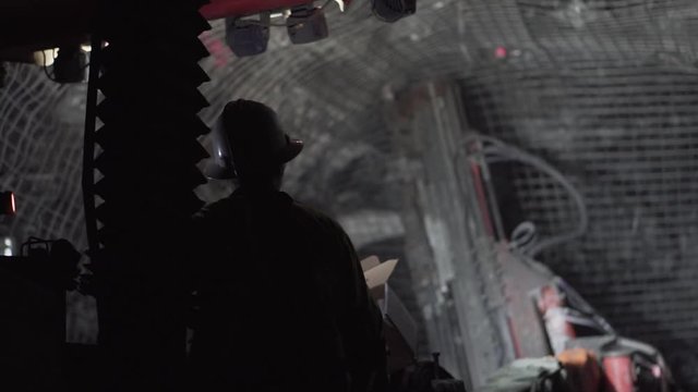 Silhouette of person operating machinery underground to drill mesh into hard rock