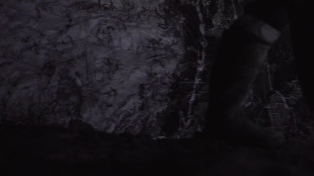 Close up of person in gumboots walking in a dark underground gold mine