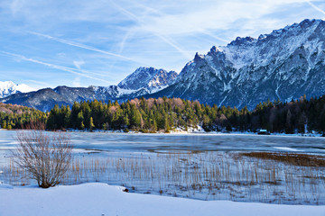 Zugefroener Bergsee mit steilen Felswänden im Hintergrund und verschneiter Landschaft
