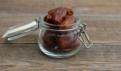 Dried pitted dates in a glass jar stand on a wooden table. Useful snack. Organic food