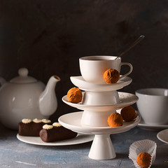 White saucer pyramid with cup of tea on top decorated with chocolate truffles on surved dessert table on dark background. Creative concept, restaurant, candy shop. Square for wallpaper, postcard