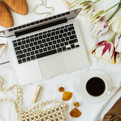Fashion / beauty blog home office desk workspace. Laptop, tulip flowers bouquet, clothes, accessories. Flat lay, top view freelancer lifestyle background.
