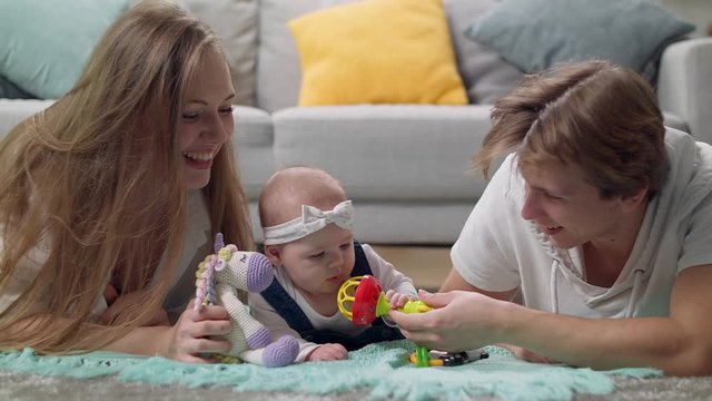 Little girl kid plays a rattle on the floor with parents