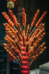 Traditional Chinese dessert Tanghulu also called bingtanghulu, is a snack of candied fruit. Hawthorn Gourd caramelized sour on bamboo skewer sold on tourist pedestrian street. Holiday winter mood