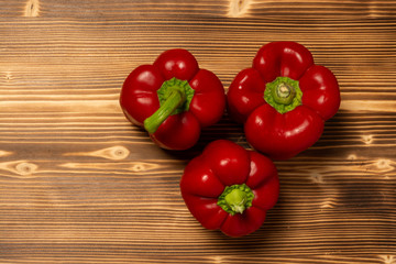 Top view of three fresh red bell peppers on wooden background  