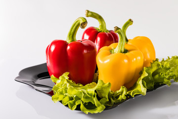 Red and yellow peppers on a black plate on a white background. Red and yellow bell peppers.