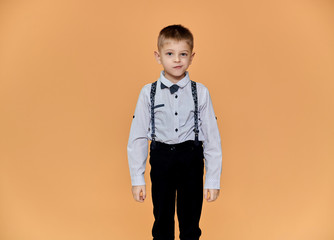 Portrait of a cute boy 10 years old schoolboy on a beige background in trousers and a shirt. Standing right in front of the camera, Shows emotions, talks in different poses.